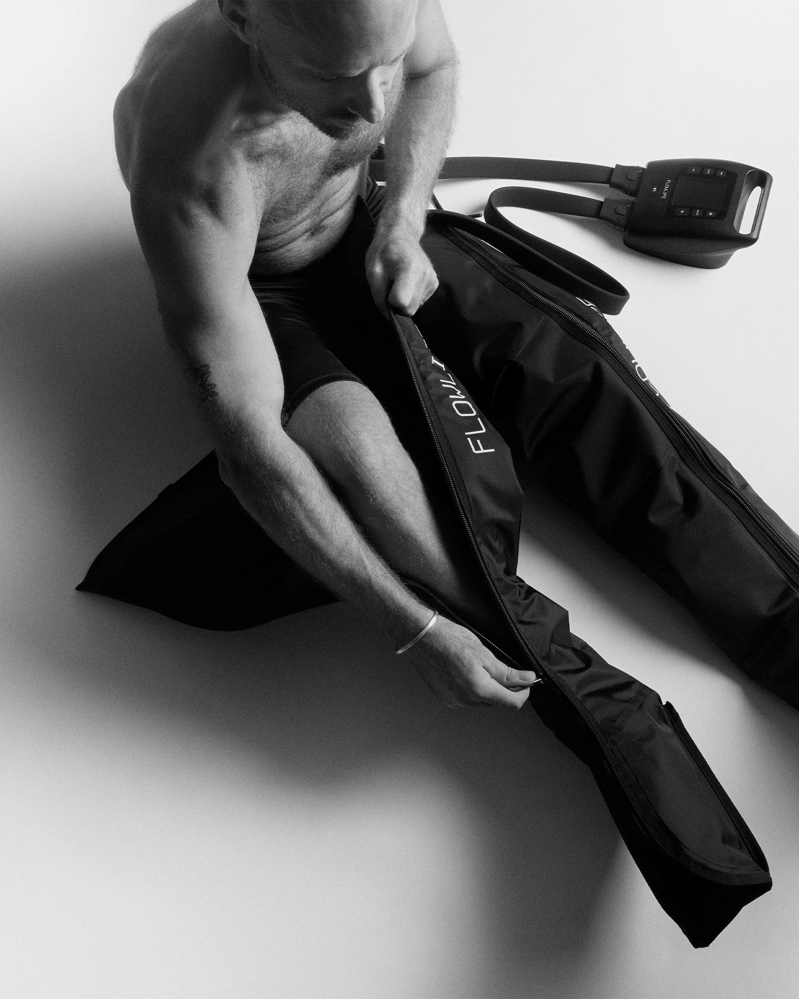 A man sitting and zipping up black Flowpression compression boots to support muscle recovery and circulation.