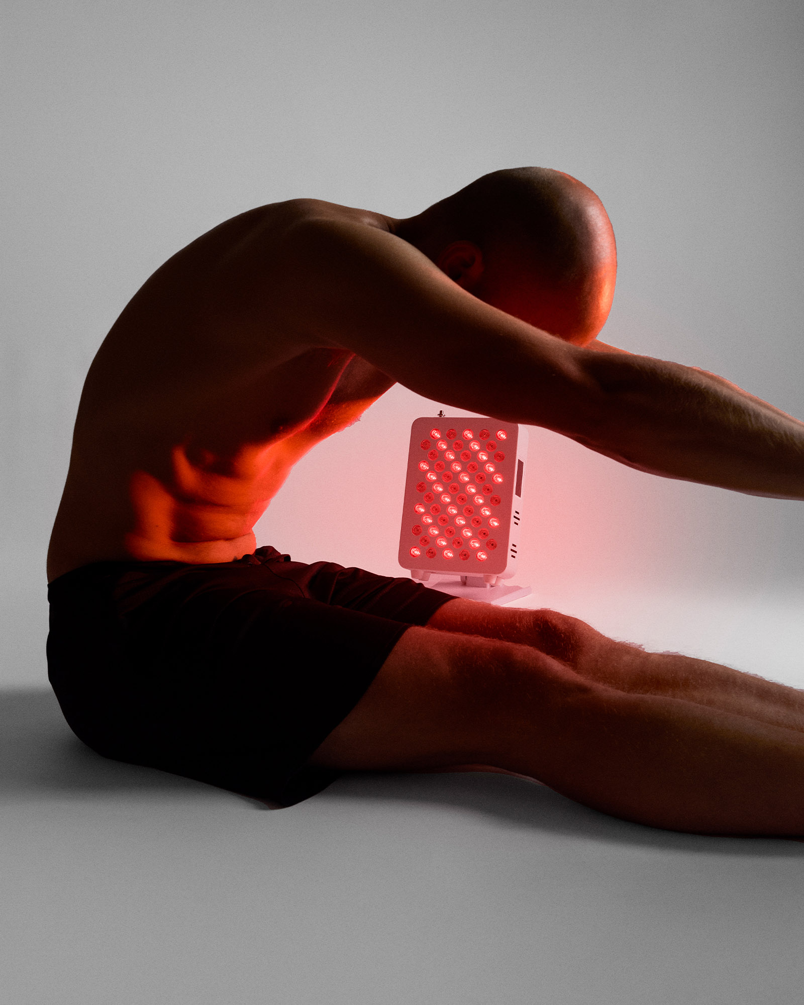 A man in a seated stretch uses the Flowlight Panel 300 Two Waves Reuse to support recovery with red light therapy.