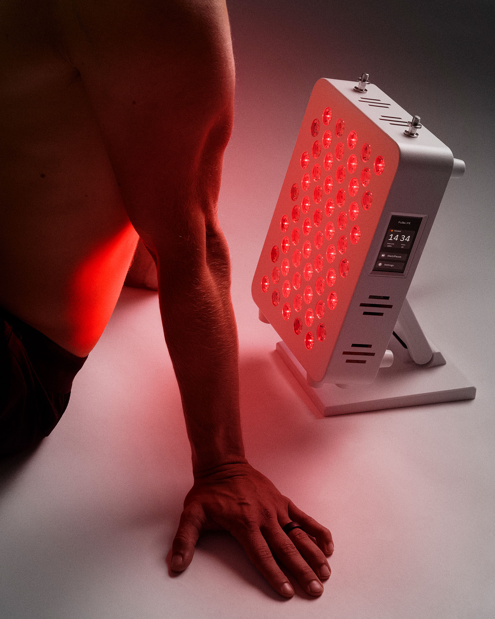 A white Flowlight Panel 300 emitting red light onto a person's back and arm to promote muscle recovery.