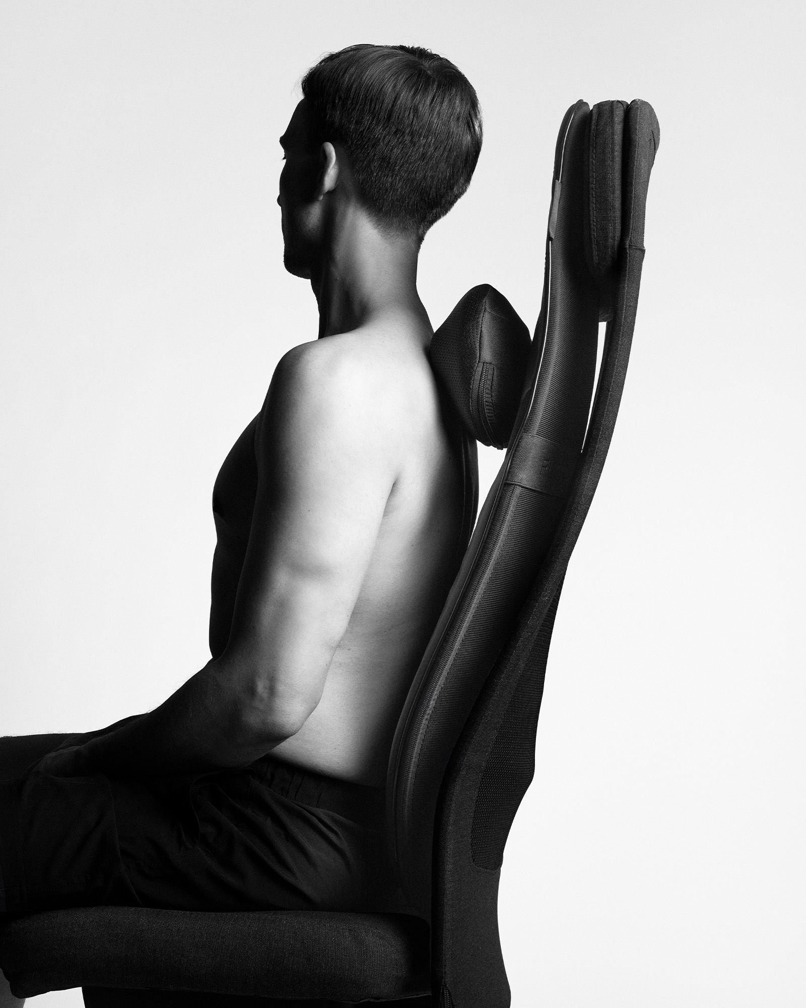 A man using a black Flowseat Pro on an office chair to relieve muscle tension and support recovery in the upper back.
