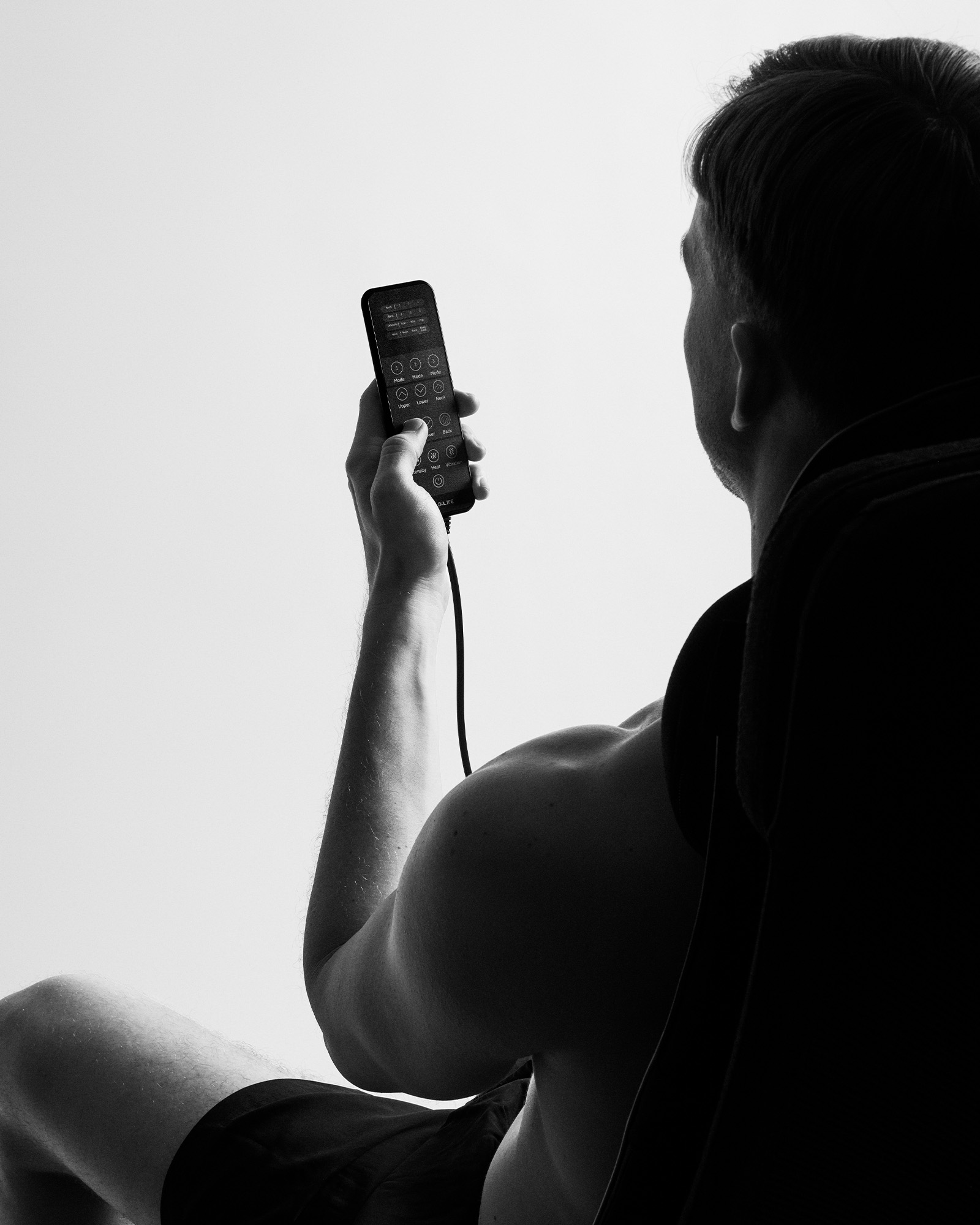 A man holding the Flowseat Pro remote control to adjust vibration massage settings for seated muscle recovery.
