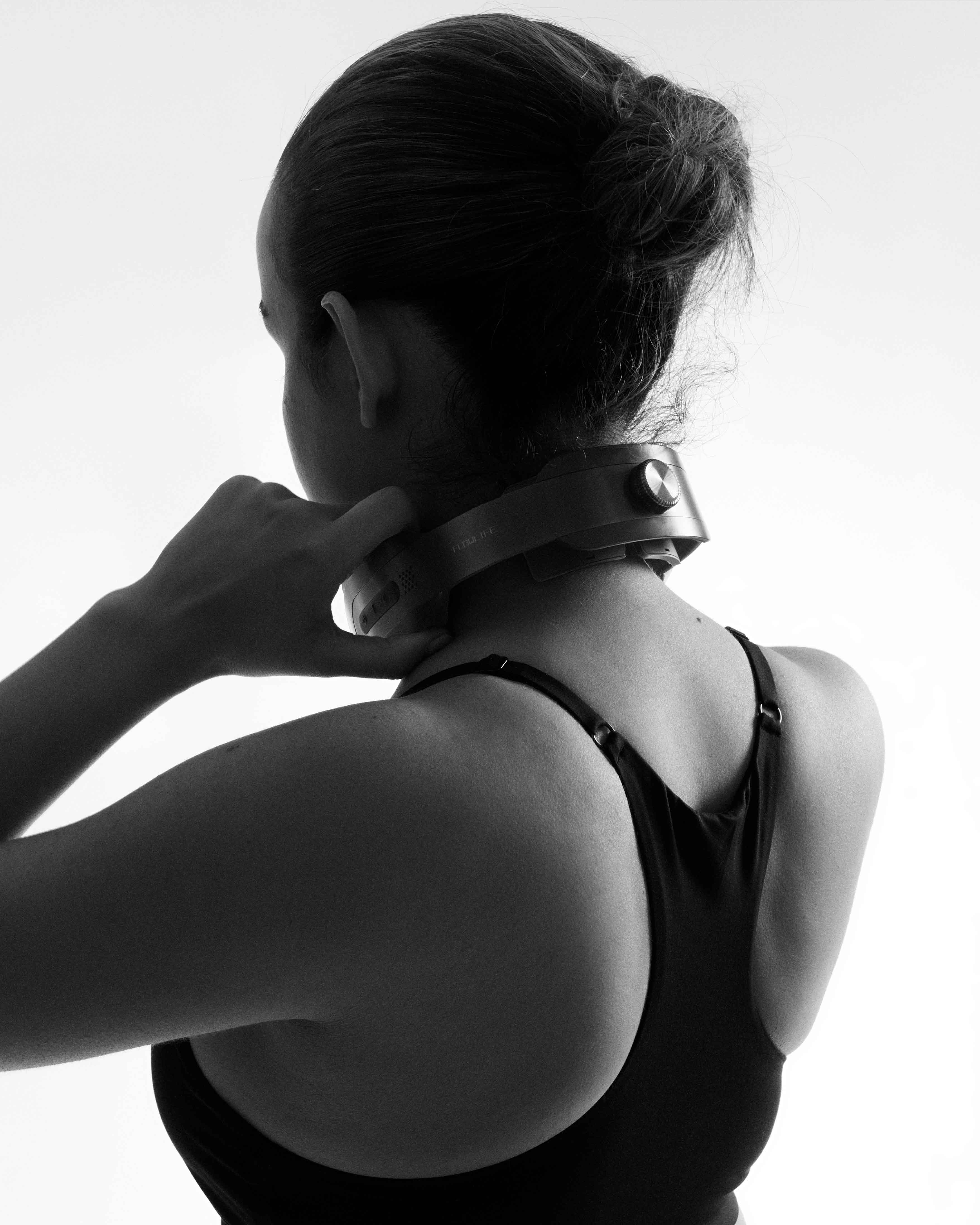 A woman wearing the Flowtens Neck device for cervical muscle recovery and tension relief, shown from behind.