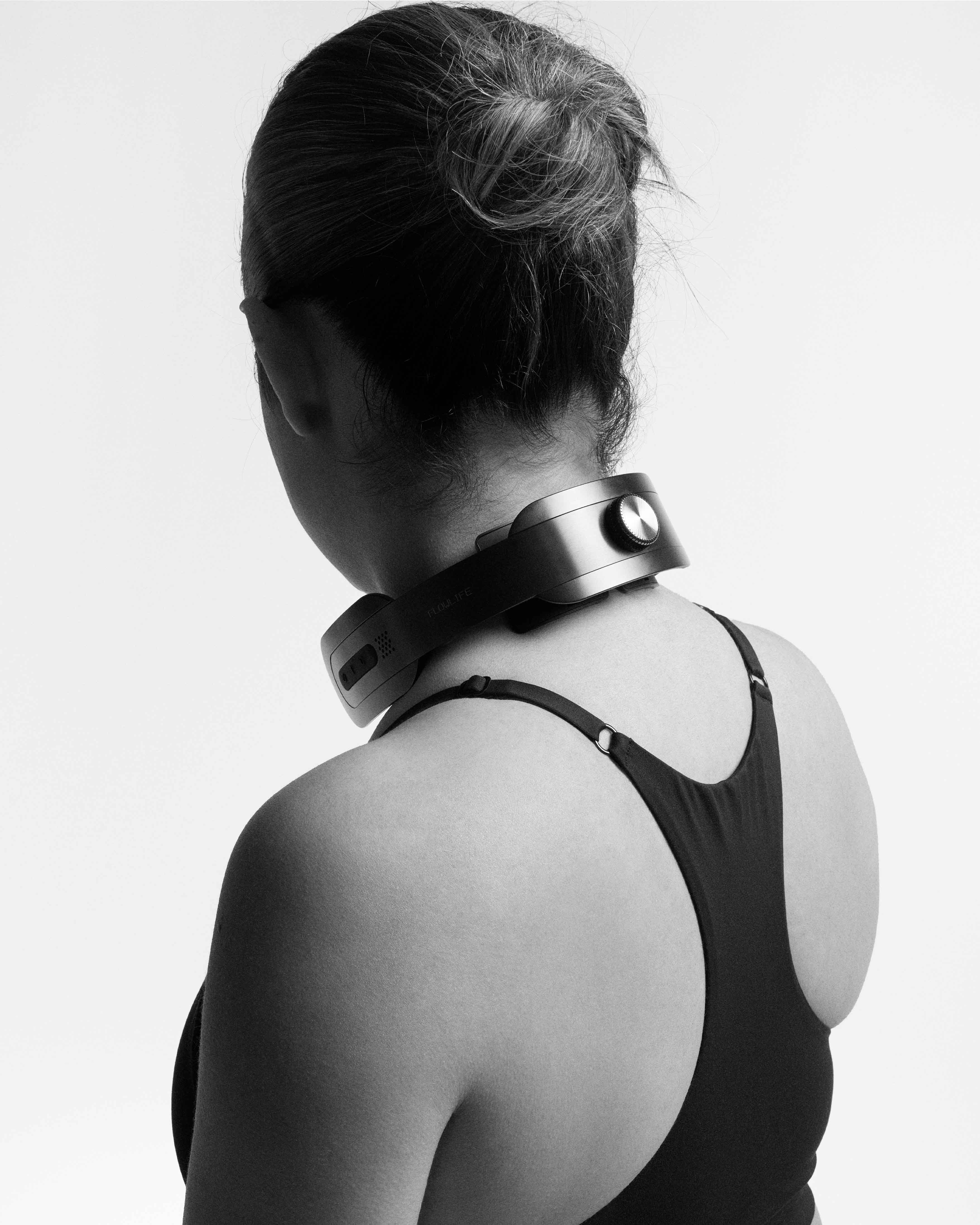 Rear view of a woman wearing the black Flowtens Neck device for cervical muscle recovery and neck relief.