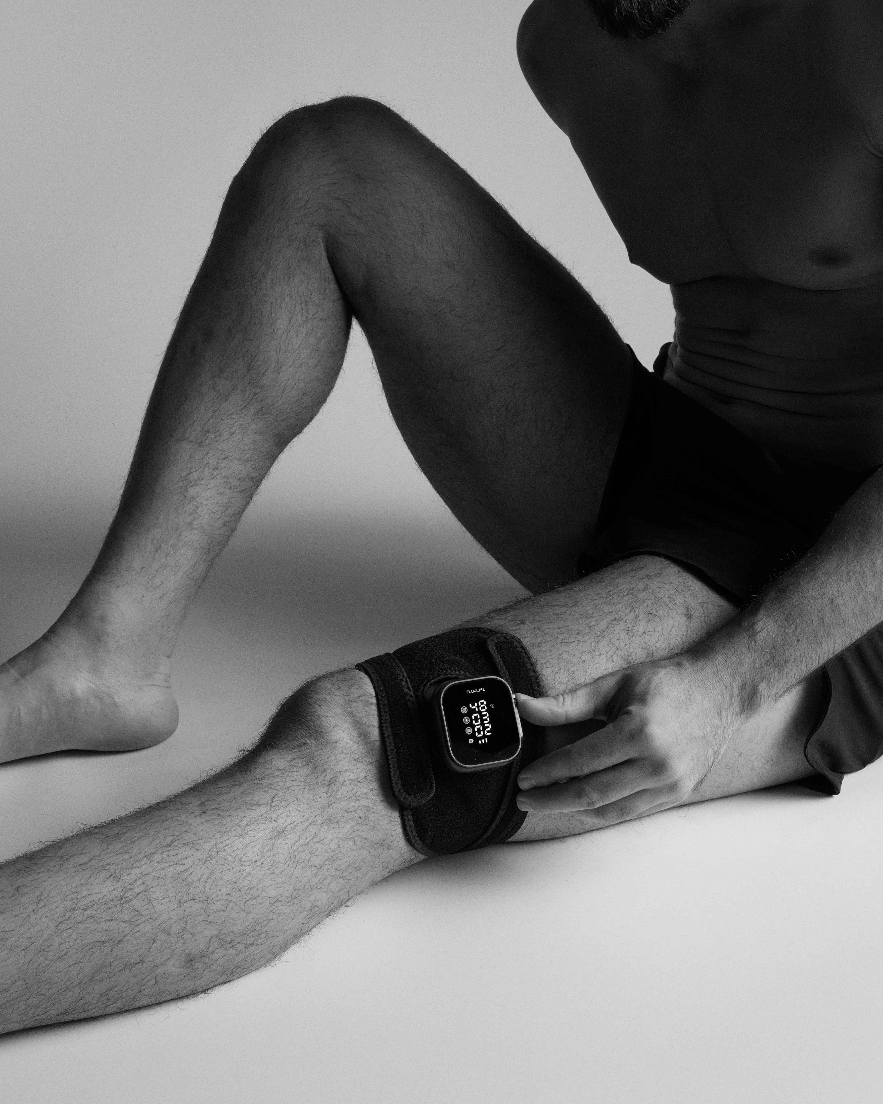 Flowtherma Spot Reuse with its digital interface and black strap applied to a man's knee for targeted thermal therapy.
