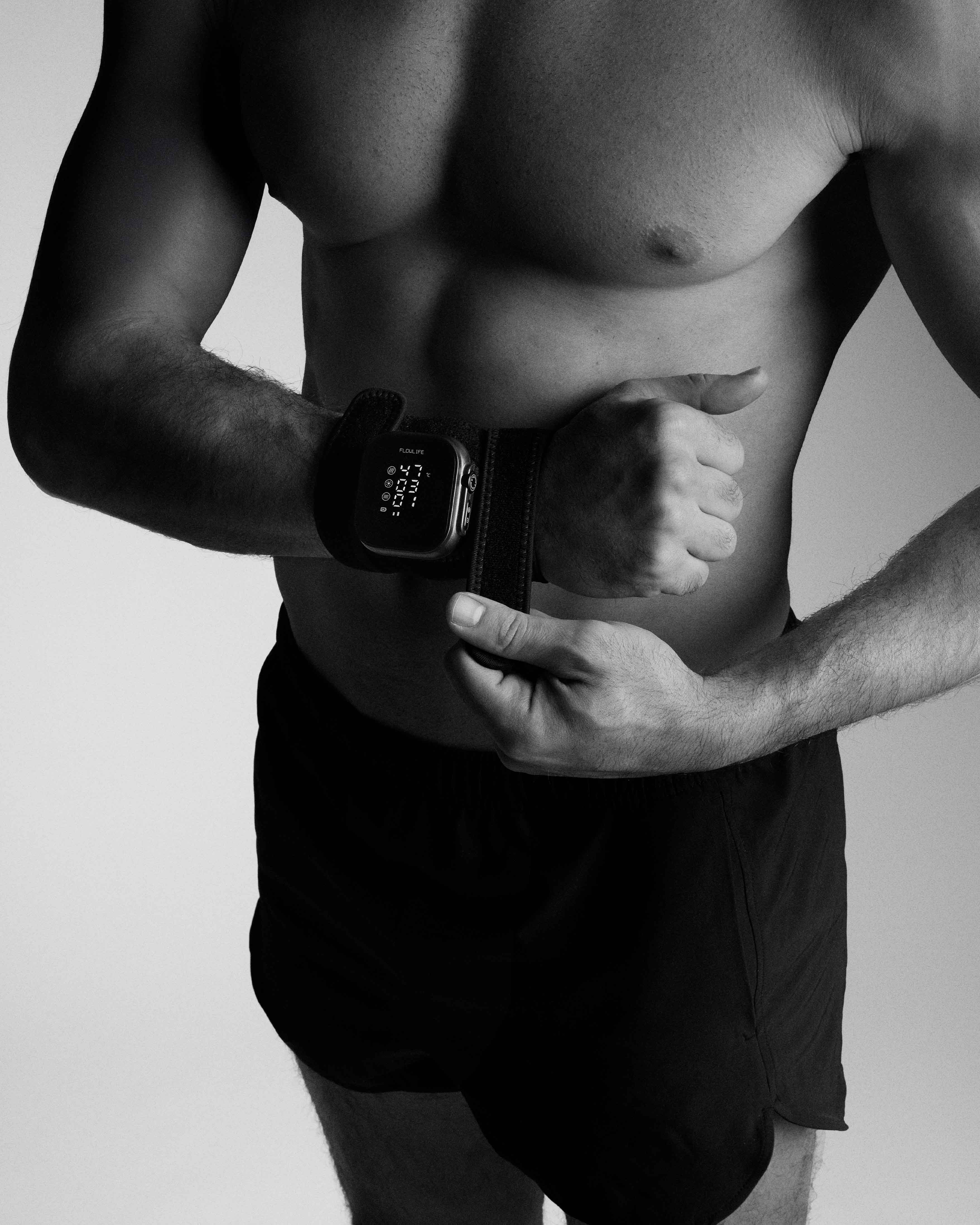 A man secures the black Flowtherma Spot to his wrist with a strap for targeted thermal recovery.