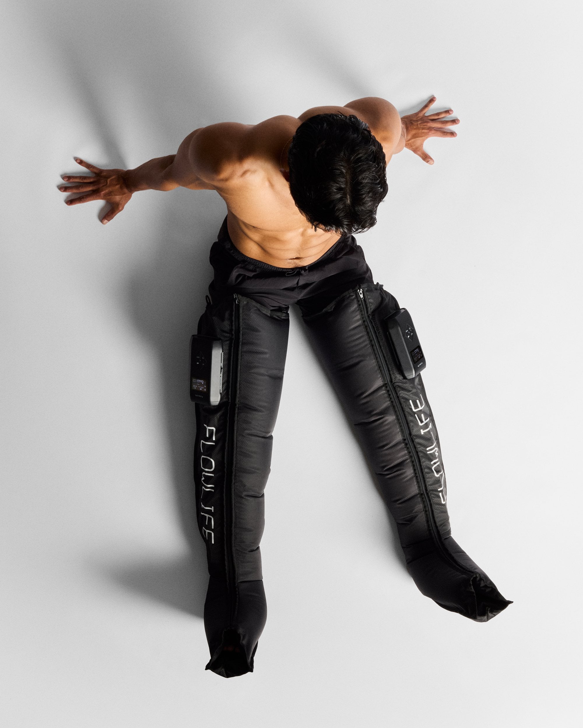 A man lying on the floor wearing both black Flowpression Boots Ultra Red Light, photographed from above in a studio.