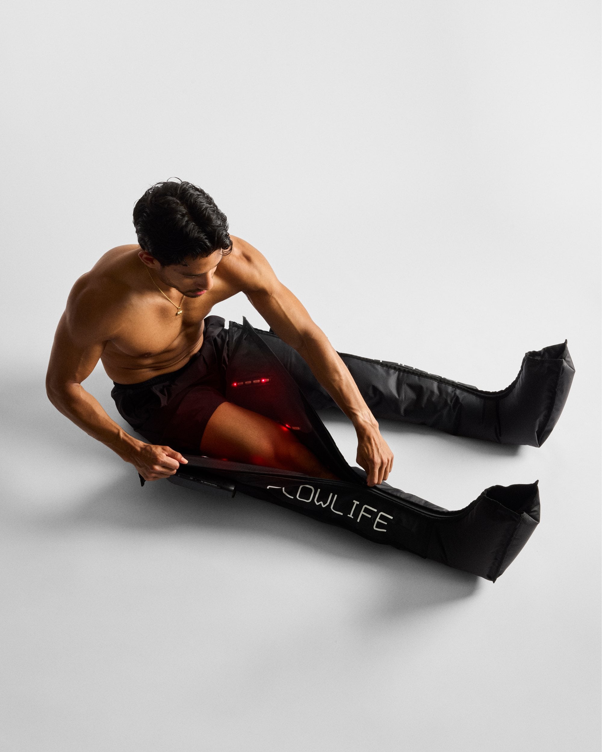 A man sitting on the floor fastening the Flowpression Boots Ultra Red Light, with red light glowing from inside the boot.