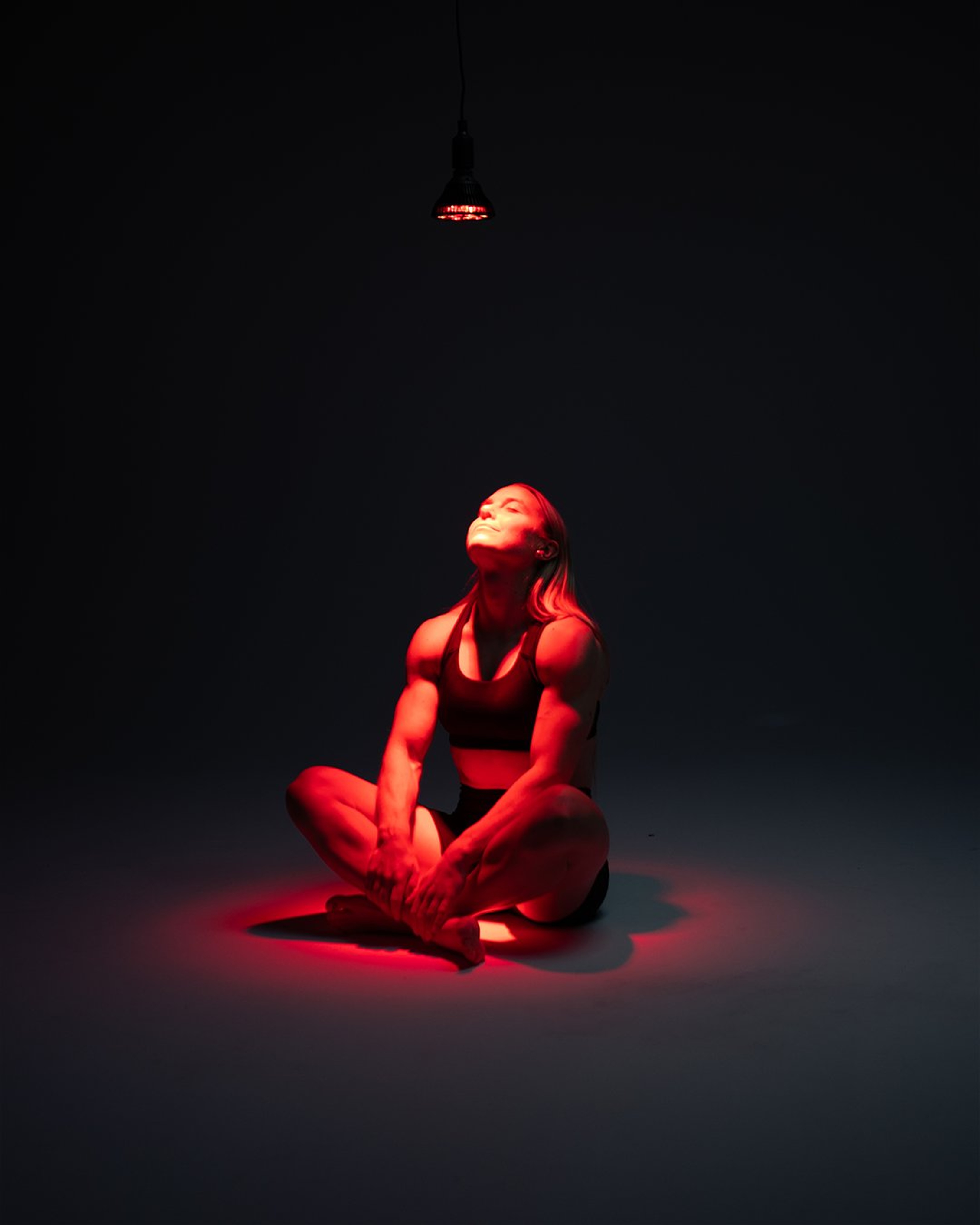 Flowlight Bulb 50 Six Waves illuminating a seated woman with red-light therapy for targeted muscle recovery.