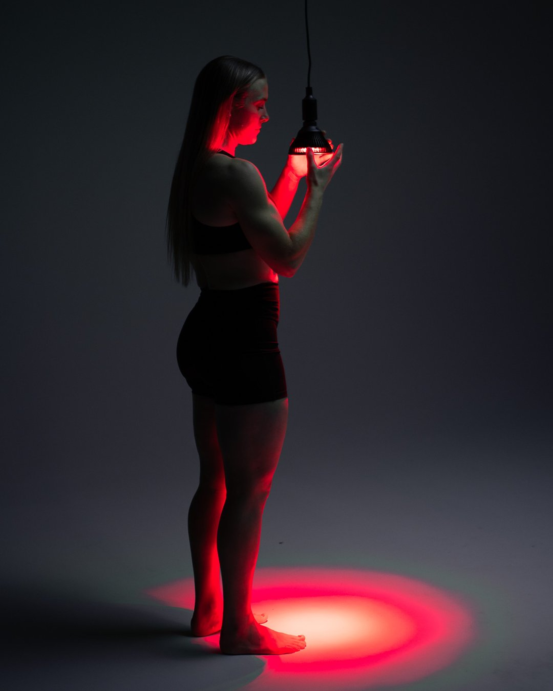 Flowlight Bulb 50 Six Waves held by a woman in black sportswear, emitting red light for targeted local muscle recovery.