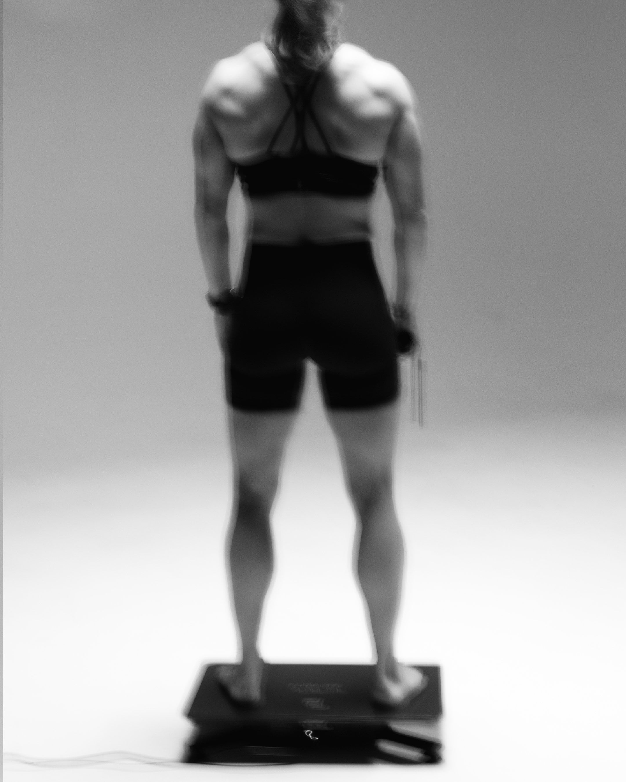 Woman standing barefoot on the Flowplate Vibe Pro, seen from behind with feet apart.