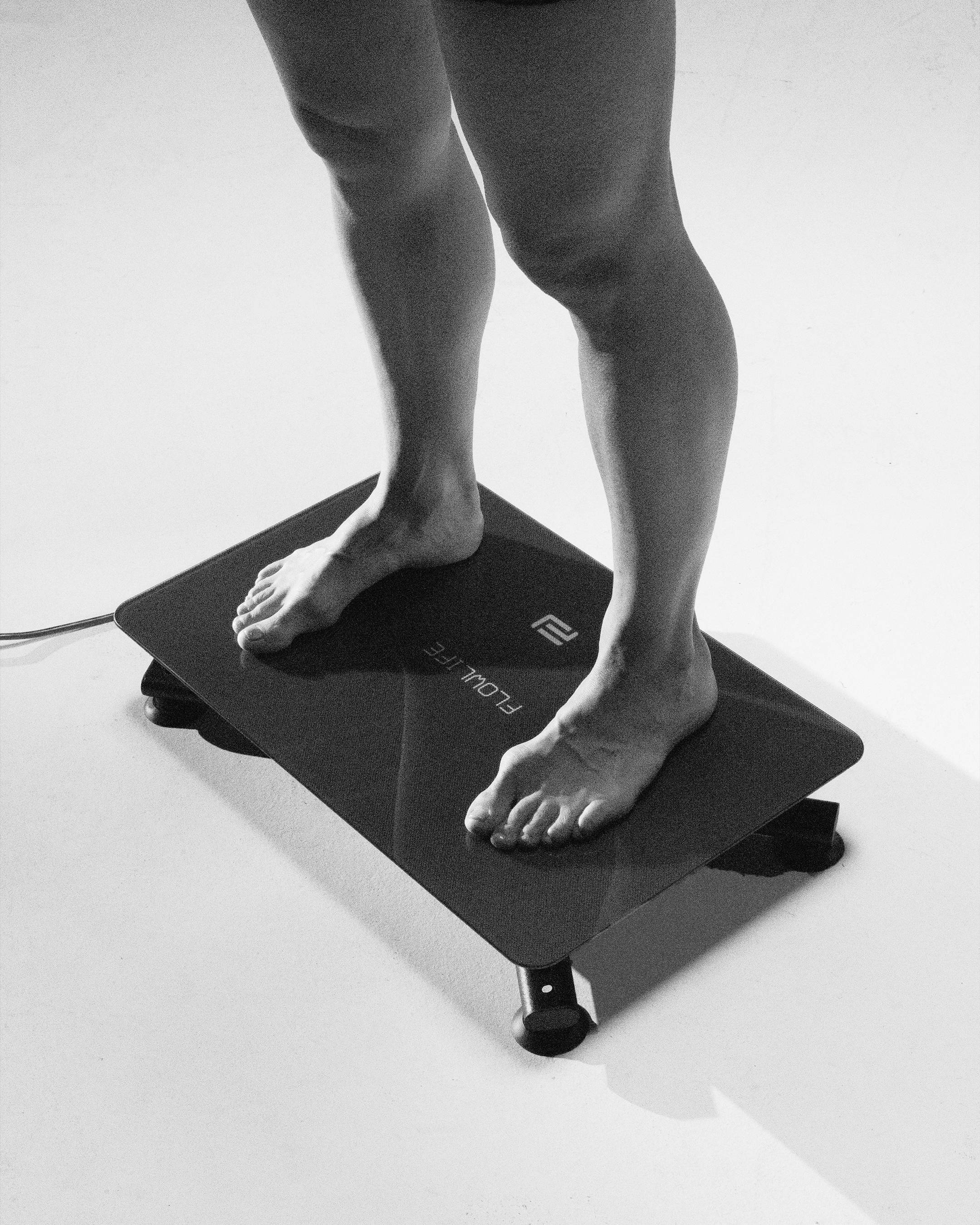 Bare feet in a wide stance on the black Flowplate Vibe Pro platform with Flowlife logo.