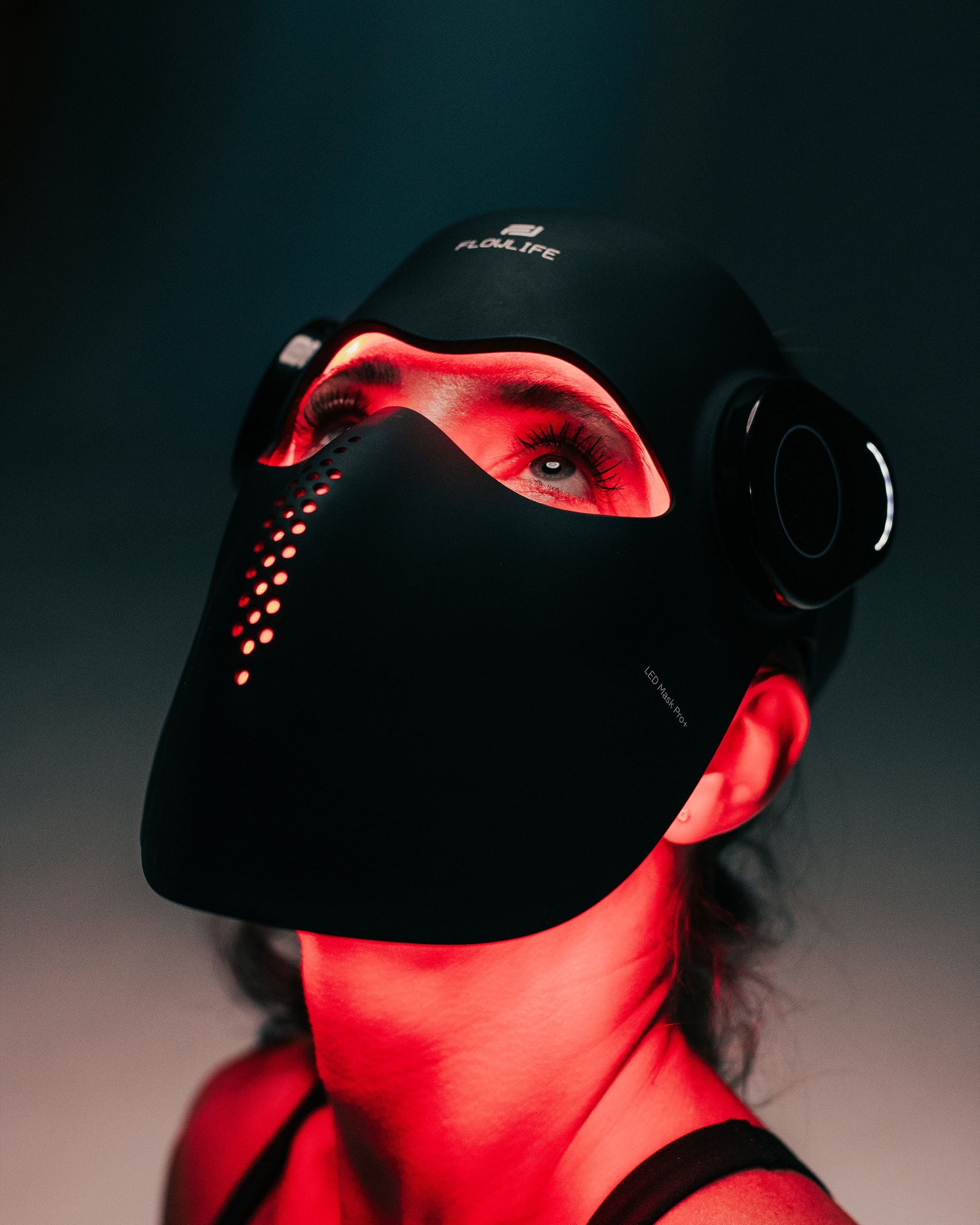 A woman tilting her head back while wearing the Flowlight LED Mask Pro+, with red light shining on her neck.