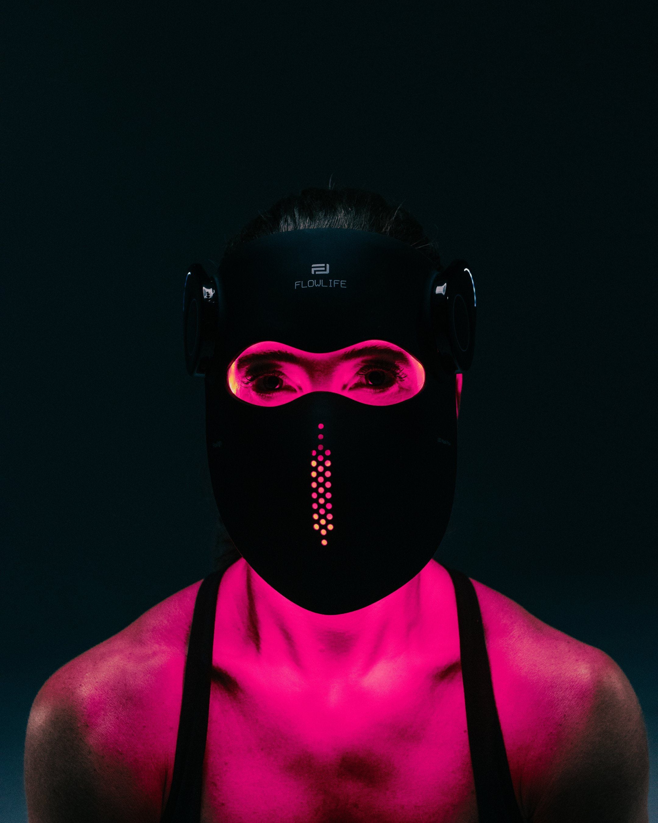A person wearing the Flowlight Laser Mask Ultra+ in pink light mode, with pink light reflecting on the neck and shoulders.